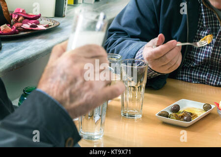Two customers drinking ouzo with olives (mezedes) inside a traditional Ouzeri Greek tavern. Stock Photo