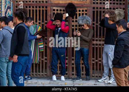 Young Uzbek Men Trying On Traditional Hats, The Registan, Samarkand, Uzbekistan Stock Photo