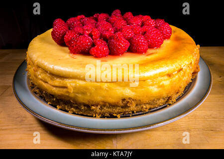 An appetising whole raspberry topped cheesecake sitting on a plate, consisting of a mascarpone cream cheese topping over a biscuit base. England, UK.