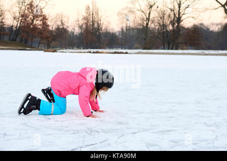 Child girl falling down on ice in snowy park during winter holidays. Wearing safety helmet. Winter children activities. Stock Photo