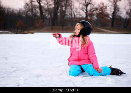 Child girl falling down on ice in snowy park during winter holidays. Wearing safety helmet. Winter children activities. Stock Photo