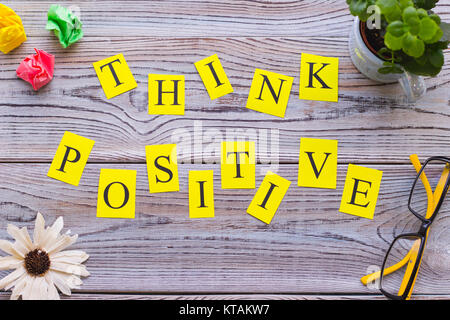Think positive inscription printed on yellow papers with a frame of office items, top view.Light wooden background. Business and motivation concept. S Stock Photo
