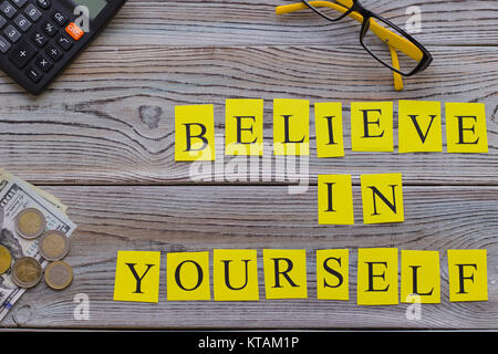 Believe in yourself printed inscription with money and office items, top view.Light wooden background. Business and motivation concept. Space for your Stock Photo