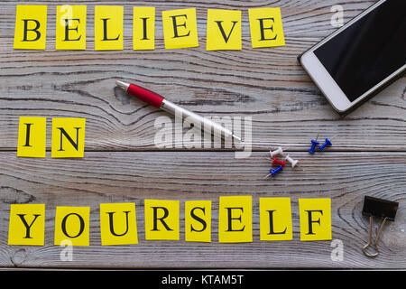 Believe in yourself printed inscription with a mobile phone, pen and pins, top view.Light wooden background. Business and motivation concept. Space fo Stock Photo