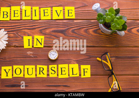Believe in yourself printed inscription with a small plant, watch and glasses, top view. Rustic wooden background. Business and motivation concept. Sp Stock Photo