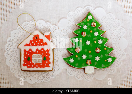 Two gingerbread cookies in the shape of the Christmas tree and small house on a white napkin background. Top view, flat lay, copy space Stock Photo