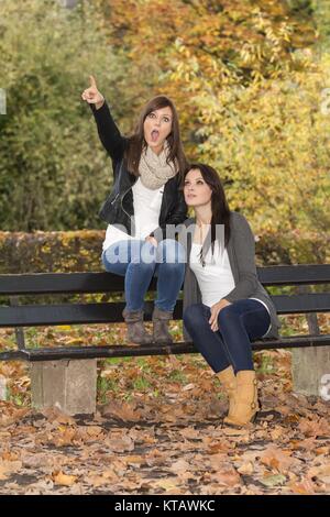 two beautiful women on the bench in colorful autumn nature Stock Photo