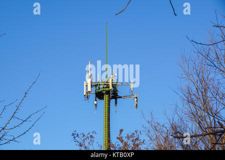 Steel telecommunication tower with antennas over blue sky and trees Stock Photo