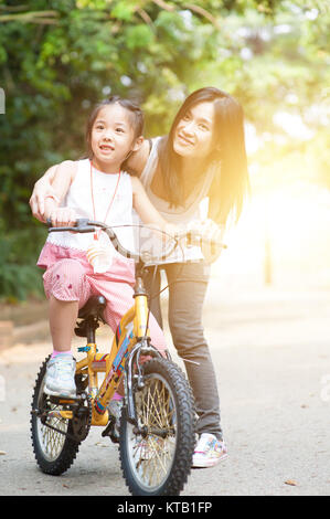 Child learning to bike with help of mother outdoor. Stock Photo