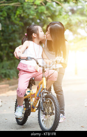 Child riding bike and giving kiss to mother, outdoor park. Stock Photo