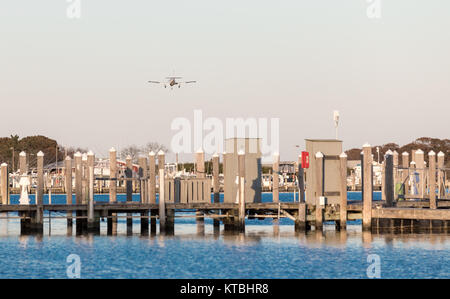 small single engine plane on an approach to montauk's airport, flying over a marina Stock Photo