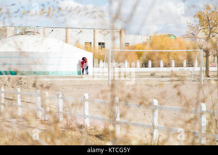 A young couple in Mongolia steal a kiss framed by autumn leaves