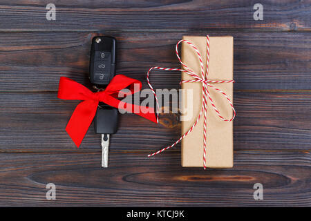 Close-up view of car keys with red bow as present on wooden background. Stock Photo