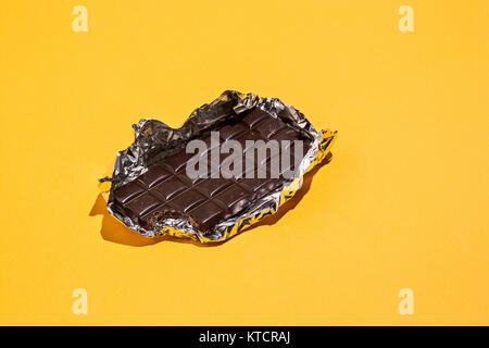 Bitten Chocolate bar in foil isolated on yellow background. Stock Photo