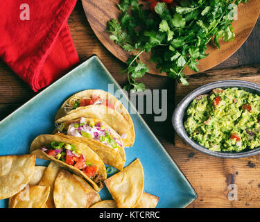 Overhead shot of several homemade tacos. Served with fresh cilantro, guacamole and tomatoes. Stock Photo
