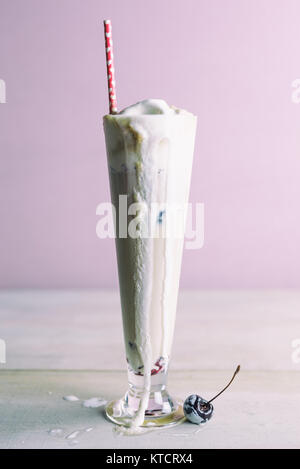 Messy, tall root beer float melting with fallen fresh cherry garnish. Vanilla ice cream dripping down the sides. Pastel background. Copy space. Stock Photo