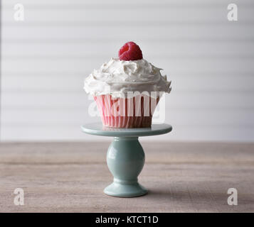 Pink cupcake with fresh raspberry garnish being served from a mini cake plate. Against a white background. Copy space. Stock Photo