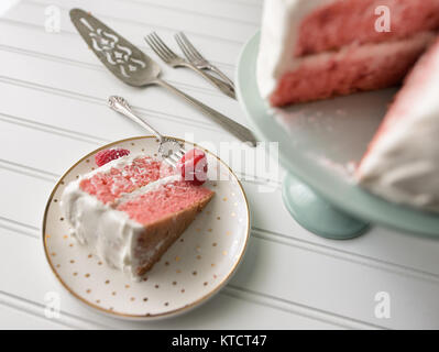 Single piece of pink raspberry cake being served on a white plate with gold polka dots. Birthday party. Fork shown with fresh raspberry. Stock Photo