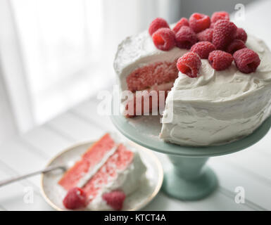 Whole raspberry cake with fresh raspberries on top being served from a mint green cake plate. Stock Photo
