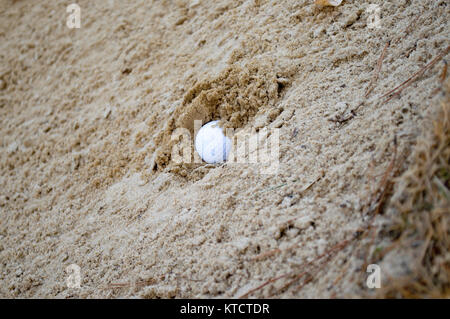 Golf ball buried in sand trap Stock Photo