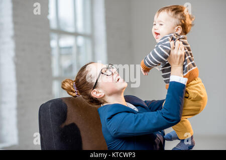 Young multitasking businessmam dressed in the suit having fun with her baby son at the office Stock Photo