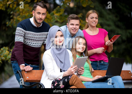 Group of young people using laptop and tablet on a park bench, having fun, talking, hanging out Stock Photo
