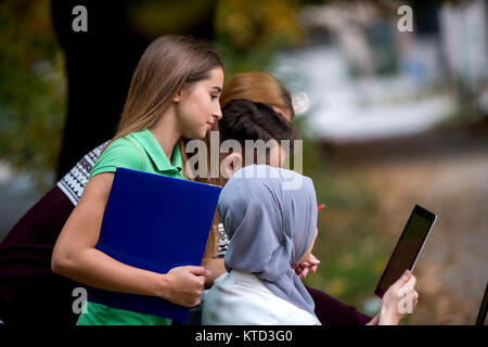 Group of young people using laptop and tablet on a park bench, having fun, talking, hanging out Stock Photo