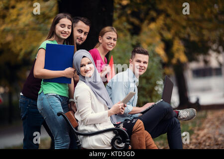 Group of young people using laptop and tablet on a park bench, having fun, talking, hanging out Stock Photo