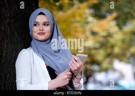 Young girl wearing hijab using talbet outside, happy Stock Photo