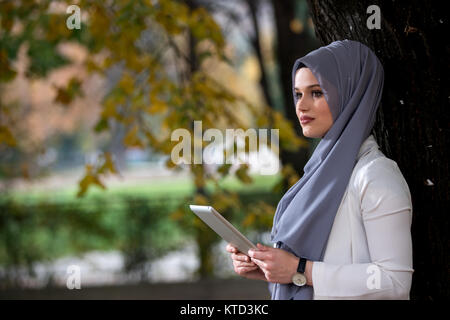 Young girl wearing hijab using talbet outside, happy Stock Photo