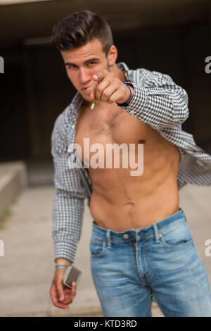 Strong and muscular young man posing on the street. He wears a shirt with brown stripes and wearing unbuttoned. Stock Photo