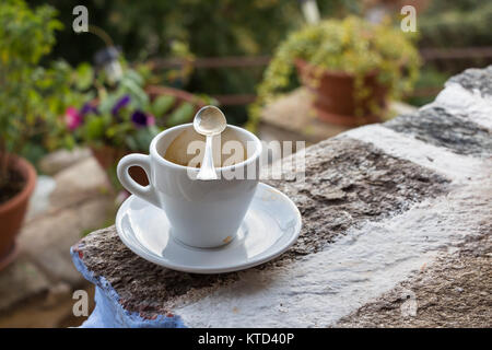 A white small cup of coffee espresso with a spoon over the cup placed in  a stone wall outdoors in Larissa, Greece. Stock Photo