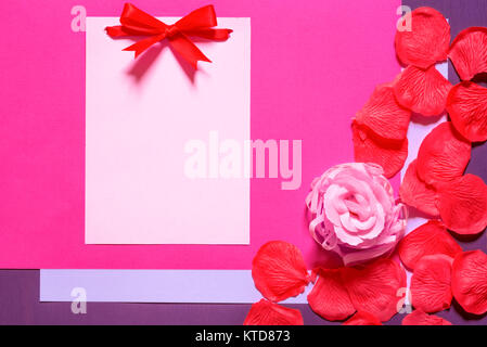 Unwritten message card tied with red bow surrounded by a pink rose and red petals made of soap, on magenta and purple paper backgrounds. Stock Photo