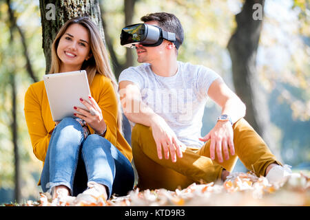 Couple sitting outside using various tech gadgets, tablet, vr, concept Stock Photo