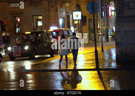 gritty urban night time Glasgow wet street life young couple a boy and a girl walking on a night out date late at night with taxi taxis Stock Photo
