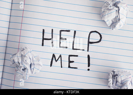 Help me!. Phrase Help Me! on notebook sheet with some crumpled paper balls on it. Close up. Stock Photo