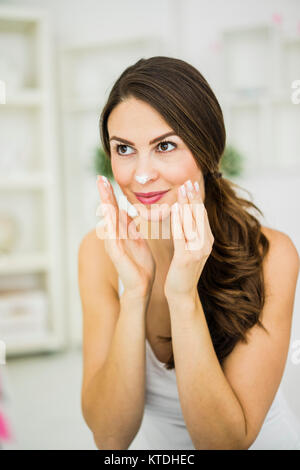 Portrait of smiling young woman creaming her face Stock Photo