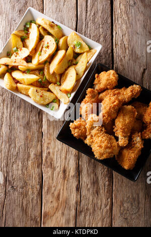 Fried chicken wings in bread crumbs and potato wedges close up on the table. Vertical top view from above Stock Photo