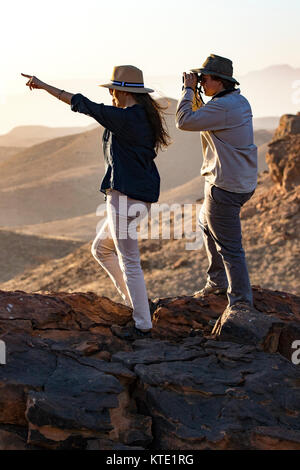Couple looking out over vast red rock landscape of Damaraland - Huab Under Canvas, Damaraland, Namibia, Africa Stock Photo