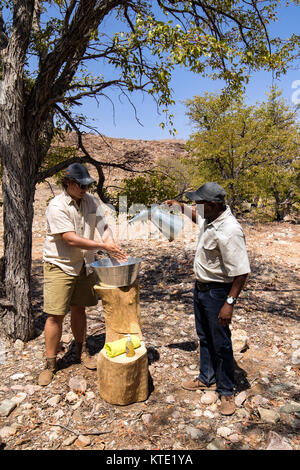 Man washing his hands in tin basin - Huab Under Canvas, Damaraland, Namibia, Africa Stock Photo