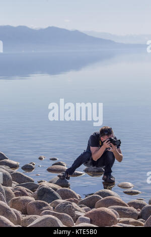 A female model on the southern shore of Issyk-Kol in Kyrgyzstan, with the mountains of the north shore reflected in the background. Stock Photo