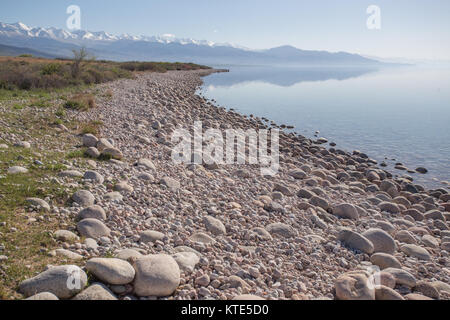 Reflections of mountains in the still waters on the southern shore of Issyk-Kol Lake in Kyrgyzstan. Stock Photo