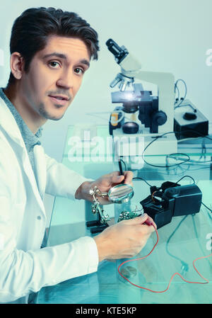 Young energetic male tech fixes electronic device, shallow DOF, focus on the eyes, this image is toned Stock Photo