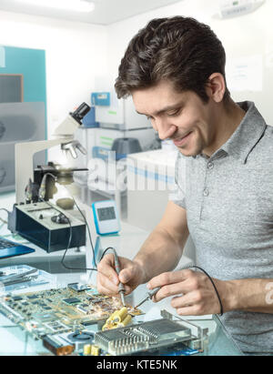 Young energetic male tech or engineer repairs electronic equipment in research facility. Shallow DOF, focus on the face and left hand of the worker. Stock Photo