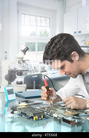 Young energetic male tech or engineer repairs electronic equipment, focus on the solrer tip and eyes Stock Photo