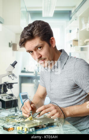 Young energetic male tech fixing motherboard looks at the viewer. Shallow DOF, focus on the right eye and fingers. Stock Photo