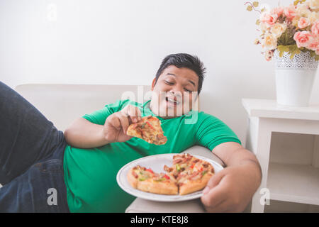 lazy overweight man eating pizza while laying on a couch Stock Photo