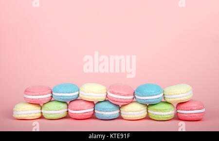 Large Macaroon cookies covered in granulated sugar on a table, two rows stacked alternating colors. pink background. Popular pastry in France. Stock Photo