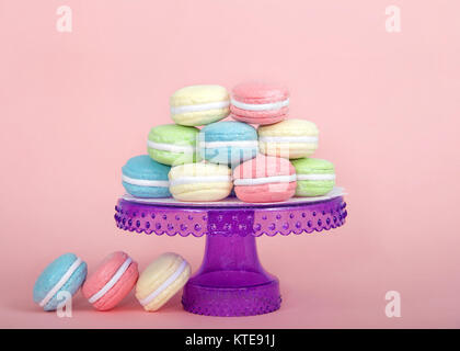 Large Macaroon cookies covered in granulated sugar on a table alternating colors stacked on a purple pedestal. Three cookies on the table. pink backgr Stock Photo