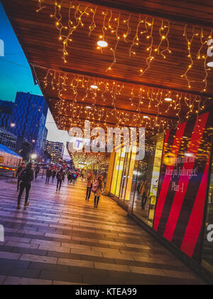 Pedestrians walking through a shopping district with holiday lights decorating the storefronts at night, Stockholm, Sweden Stock Photo
